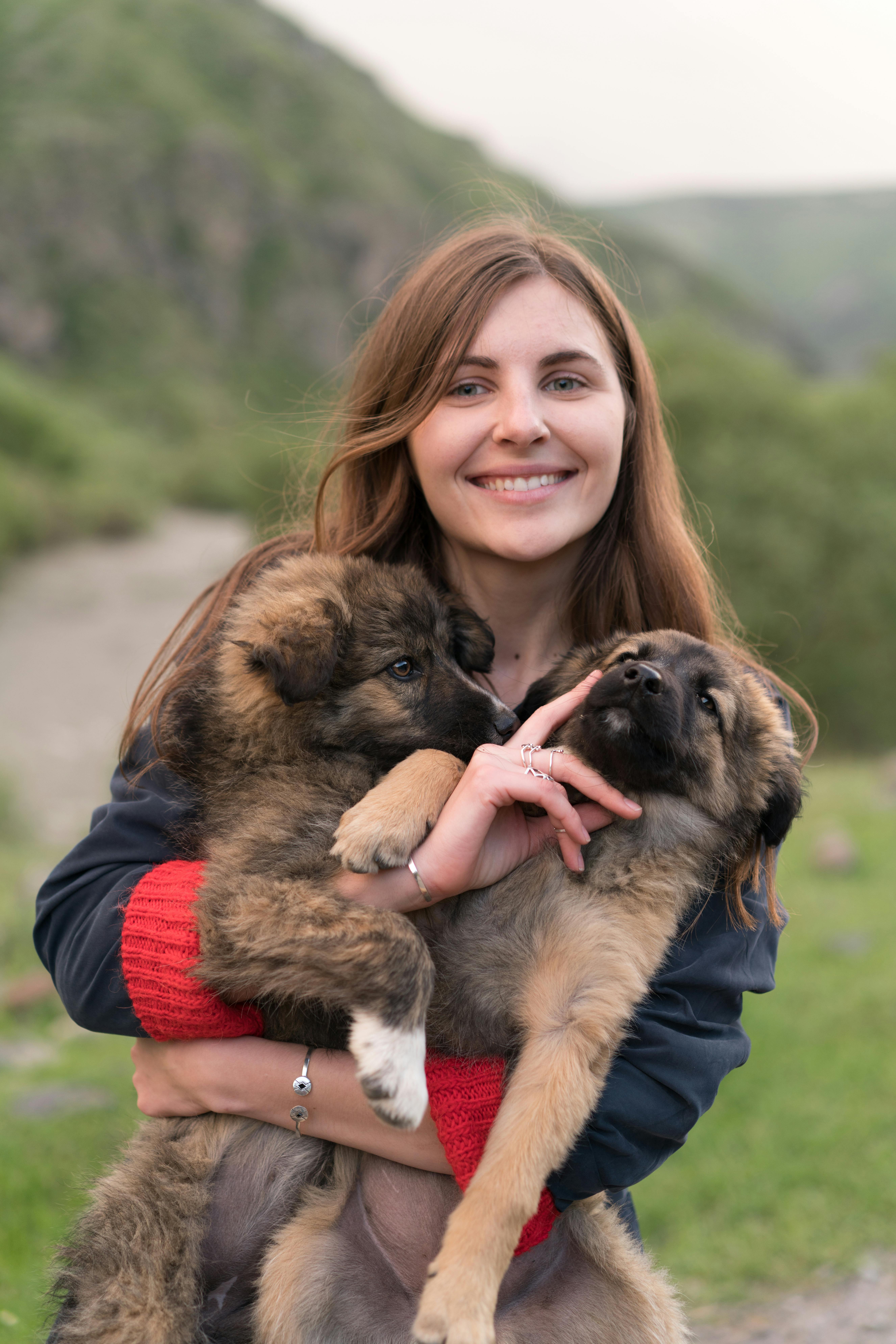 A cheerful woman holds two adorable German shepherd puppies outdoors, showcasing a loving bond with her pets.